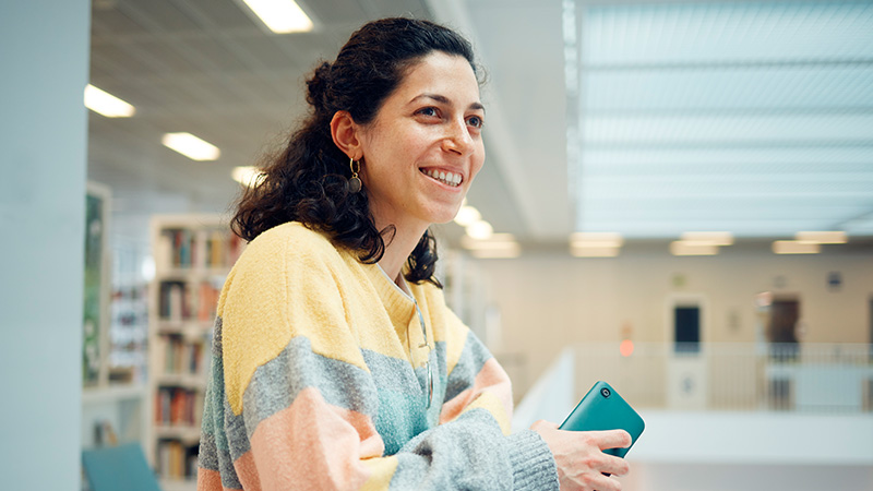 Mujer sonriendo, con una biblioteca detras