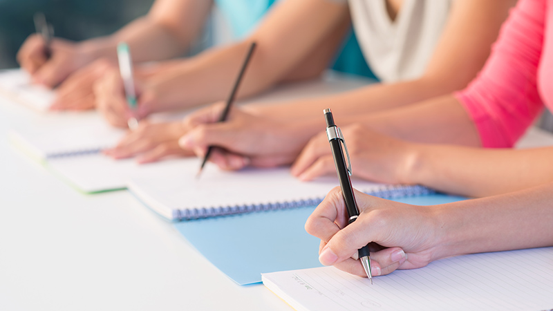 Manos de estudiantes escribiendo en cuadernos